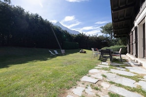 A grassy outdoor area with a mountain in the background, a stone pathway leading to a building, and outdoor seating. - Tanikel - New 100-square-meter duplex | Quiet | Mountain view | Garden (Chamonix-Mont-Blanc)