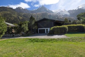 A modern house with a garage, surrounded by a well-maintained lawn and a mountain backdrop. - Tanikel - New 100-square-meter duplex | Quiet | Mountain view | Garden (Chamonix-Mont-Blanc)