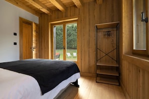 Quarto com cama, paredes de madeira, guarda-roupa e porta de vidro deslizante para área externa.