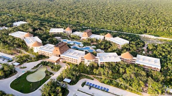 Vista aérea de un complejo turístico con varias edificaciones, una piscina y un estacionamiento.