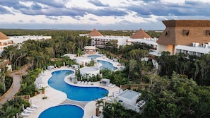 Un resort con varias piscinas, exuberante vegetación y edificios con techo de paja.