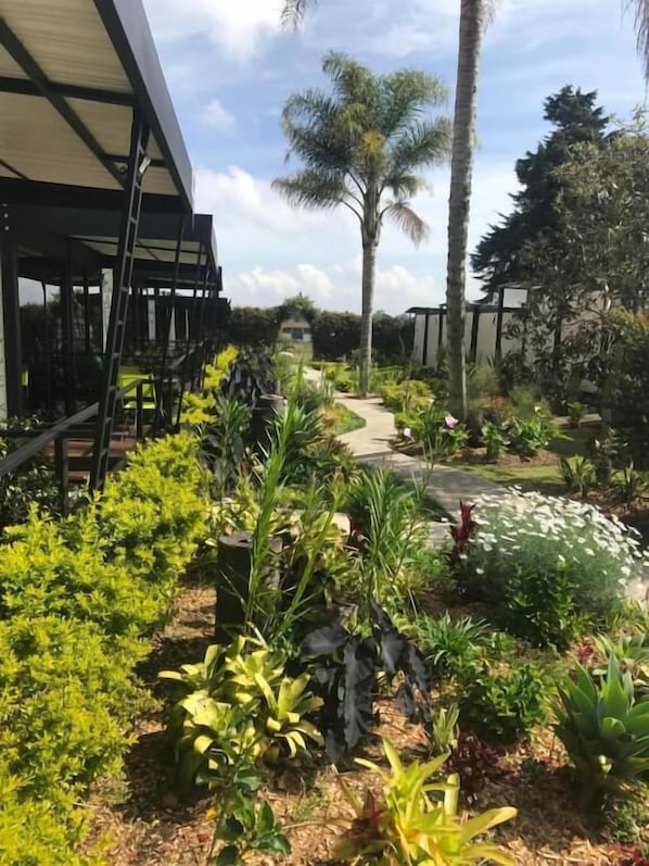 A garden with various plants and a pathway leading to a building with a covered entrance. - Hotel & Golf Isak (Rionegro)