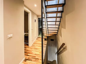 Ein modernes Interieur mit Holzboden, einer Treppe mit Glasgeländern und einer Tür zu einem anderen Raum.