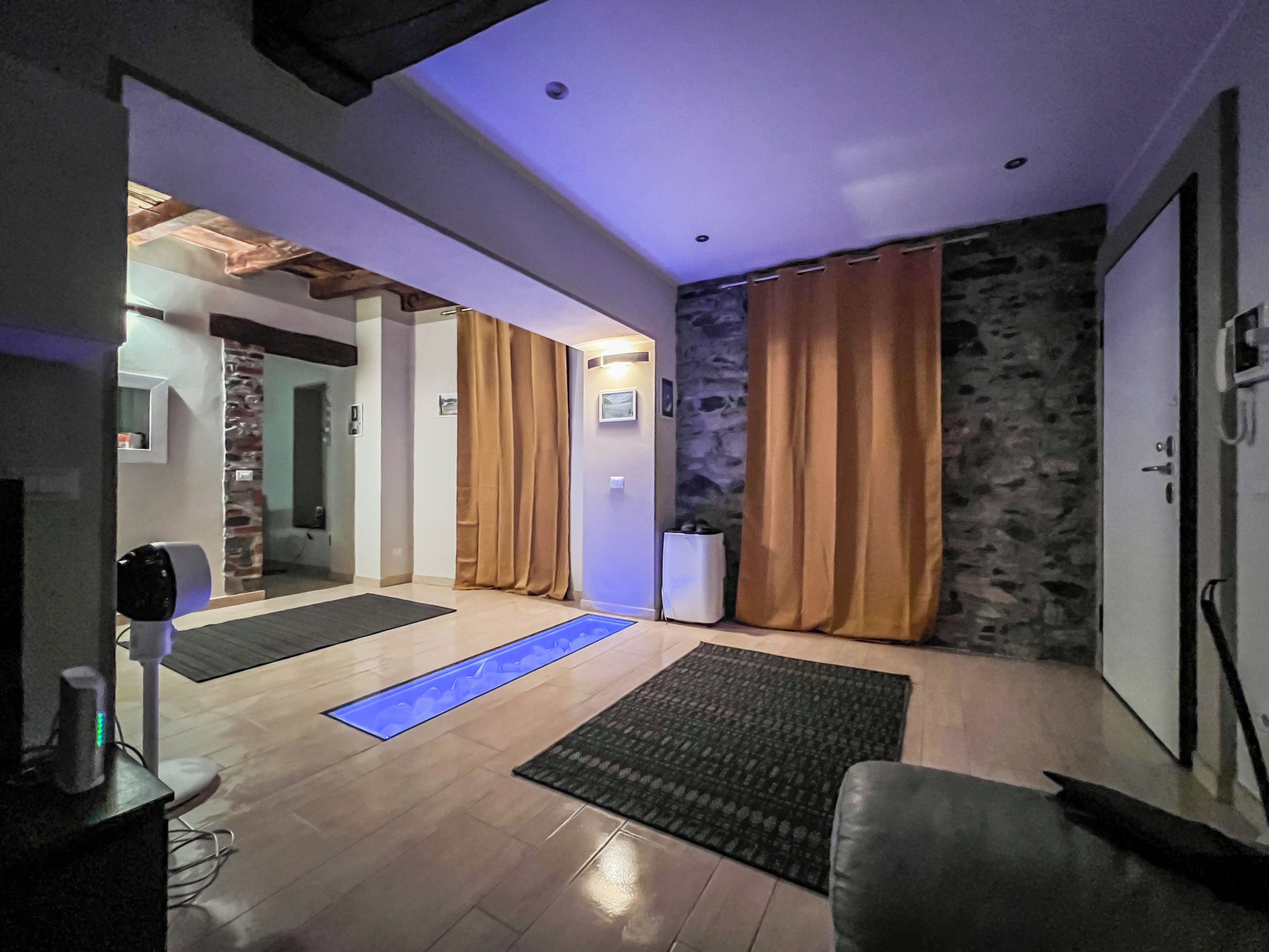 Un intérieur moderne avec un mur en pierre, des rideaux en bois et un chemin illuminé de lumière bleue menant à une porte.