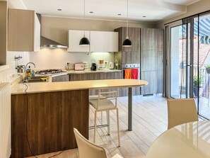 Une cuisine moderne dotée d’un îlot central, d’un coin repas et d’une porte-fenêtre coulissante donnant sur l’extérieur.