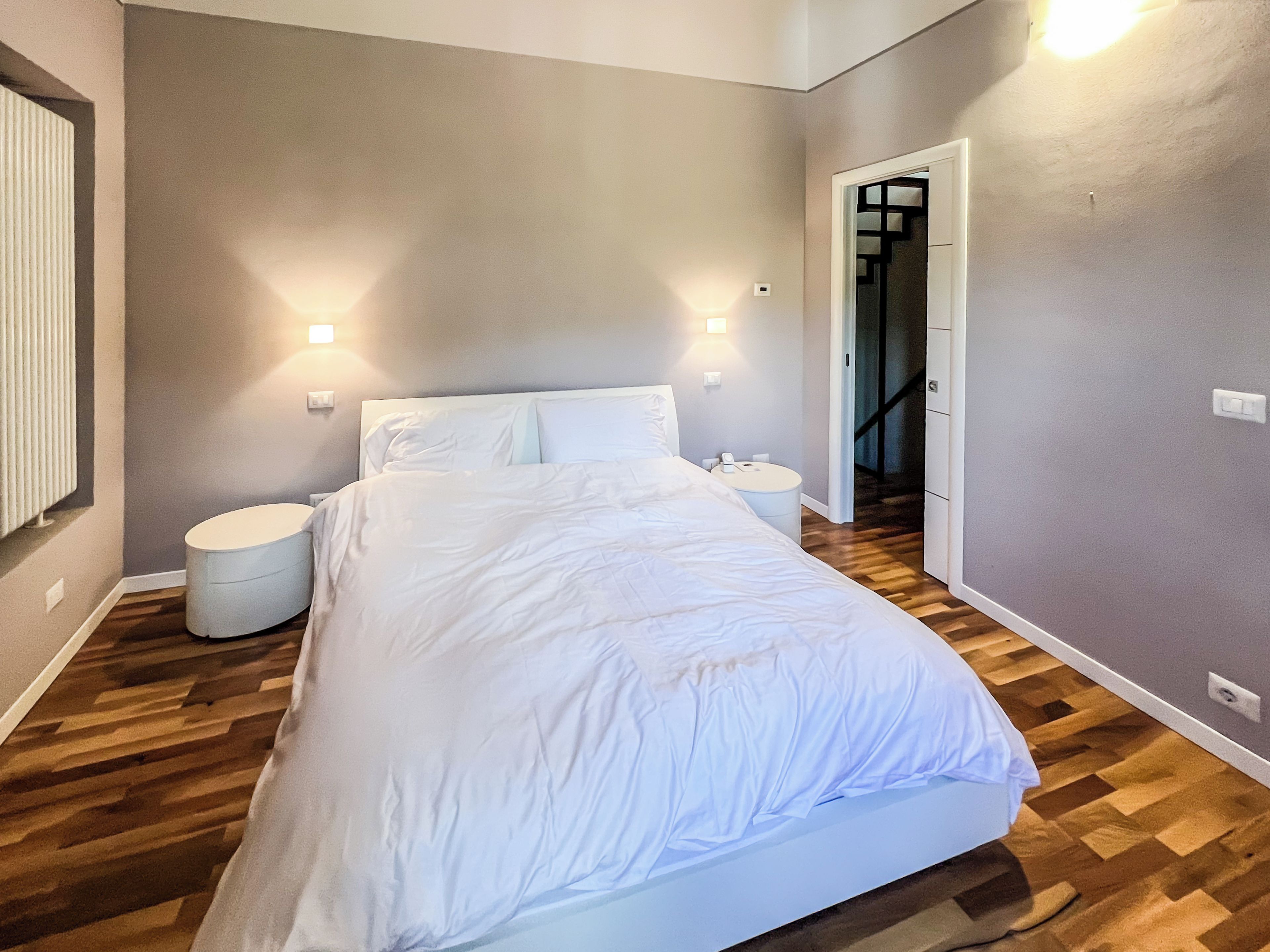 Een slaapkamer met een bed, twee nachtkastjes, een rond bijzettafeltje en een wandlamp.