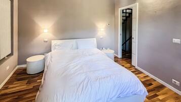 Een slaapkamer met een bed, twee nachtkastjes, een rond bijzettafeltje en een wandlamp.