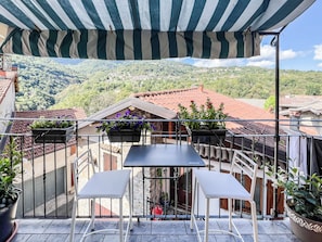 Ein Balkon mit Tisch und Stühlen, Blumentöpfen und Blick auf eine Hügelstadt.