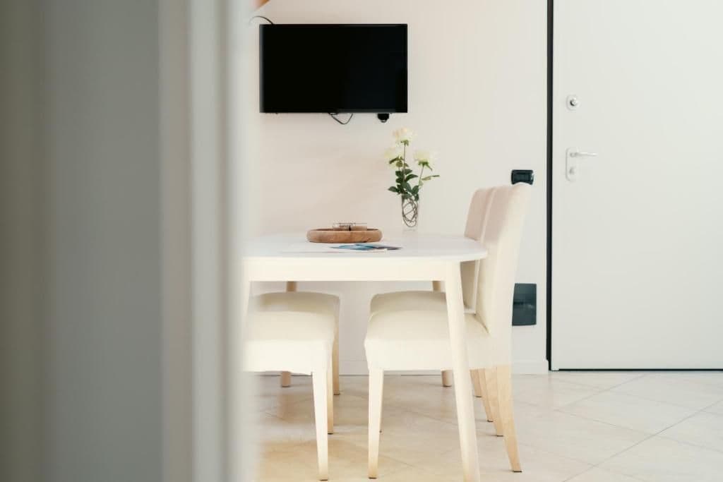 Ein Zimmer mit einem weißen Tisch, zwei Stühlen, einem Flachbildfernseher an der Wand und einer Tür mit Griff.