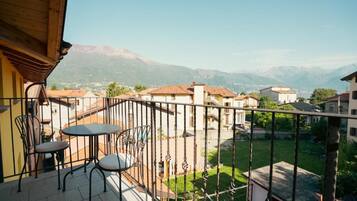 Un balcón con mesa y sillas, con vistas a una zona residencial con casas y montañas al fondo.