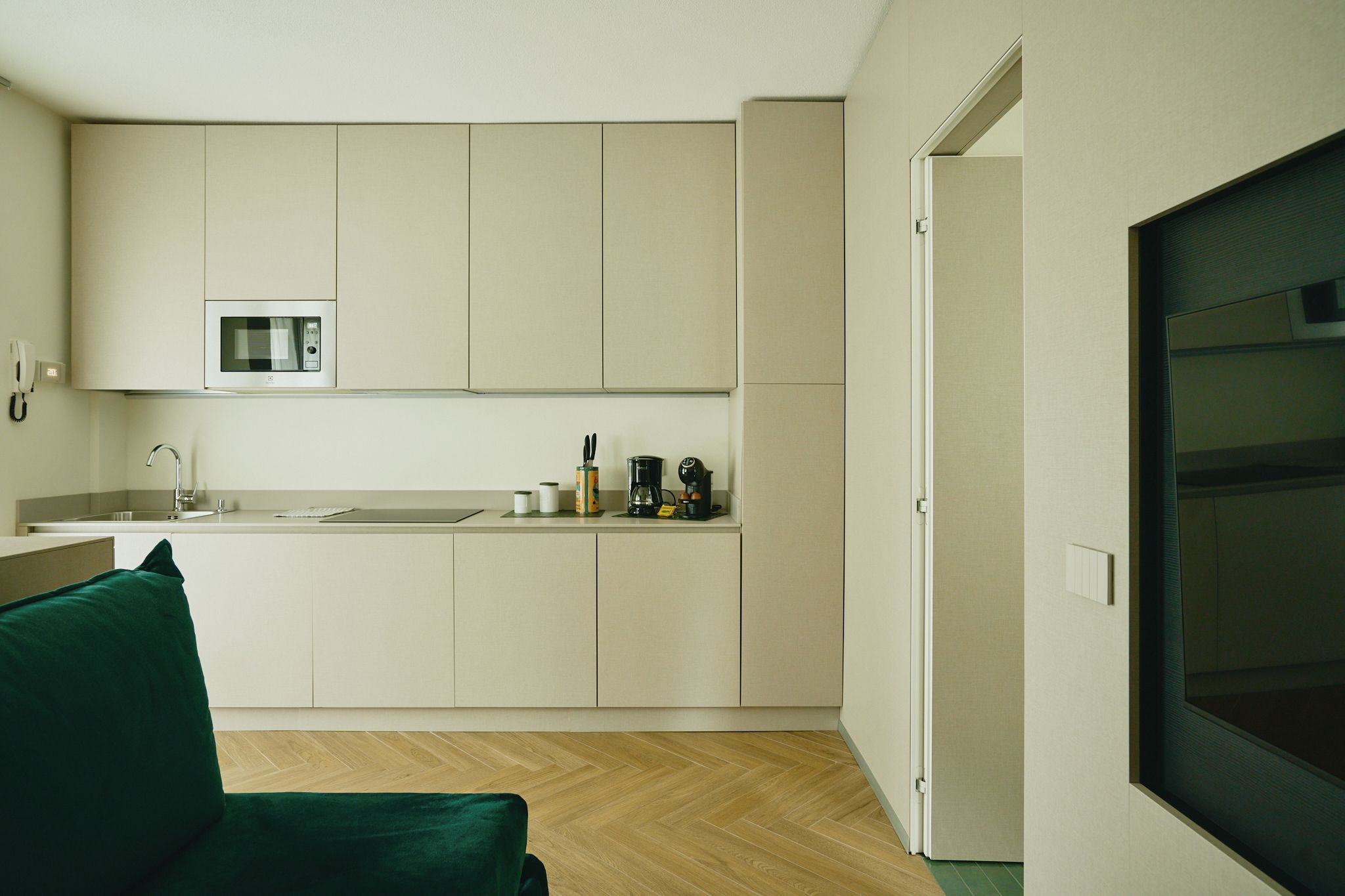 A compact kitchen with a microwave, coffee maker, and a small sink. A green chair is visible in the foreground.