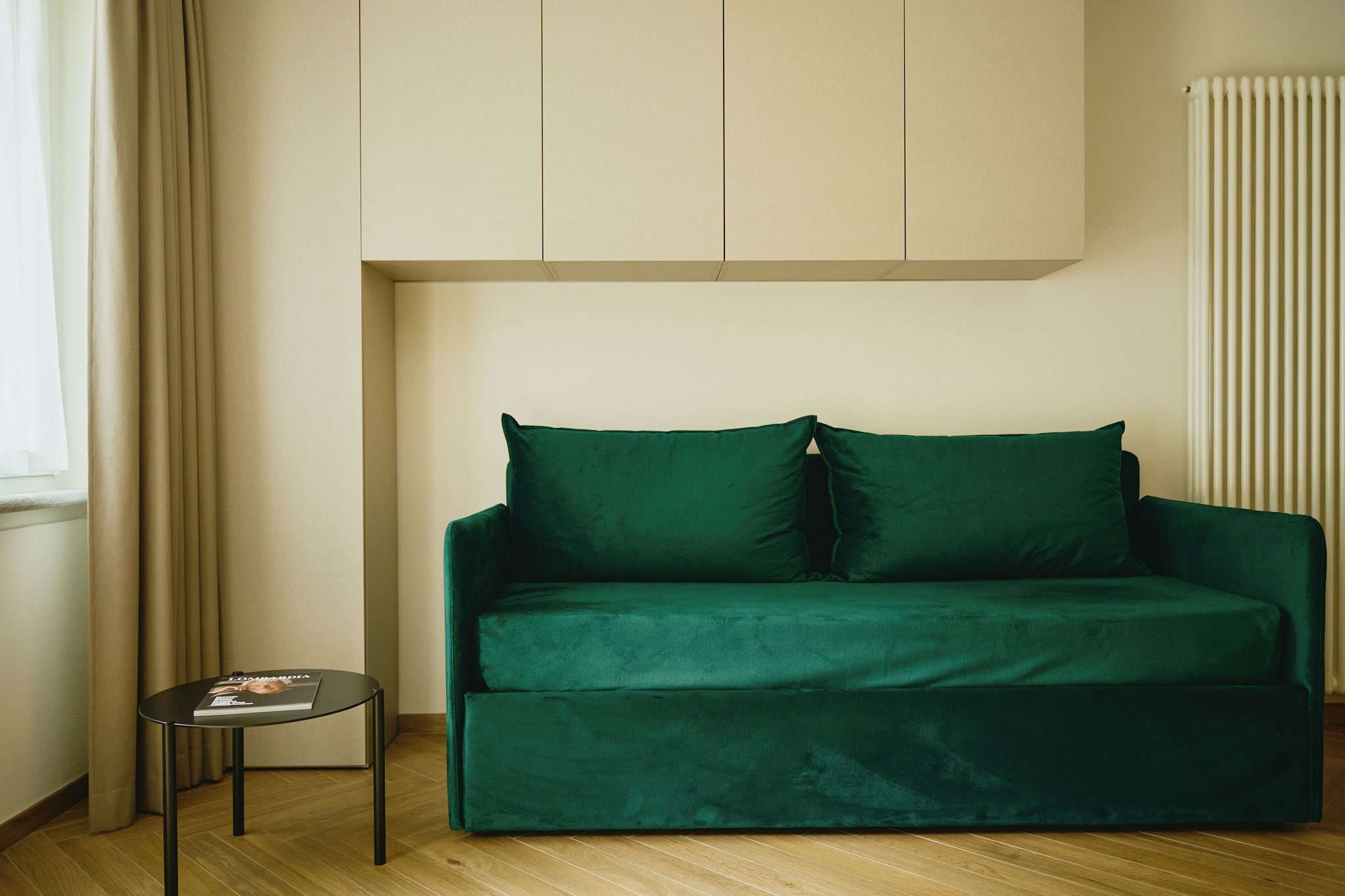 Une pièce avec un canapé vert, une petite table ronde sur laquelle se trouve un magazine et un radiateur.