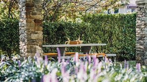 A stone bench with a table in a garden with green foliage and a stone wall. - Residence Antico Torchio (Dervio)