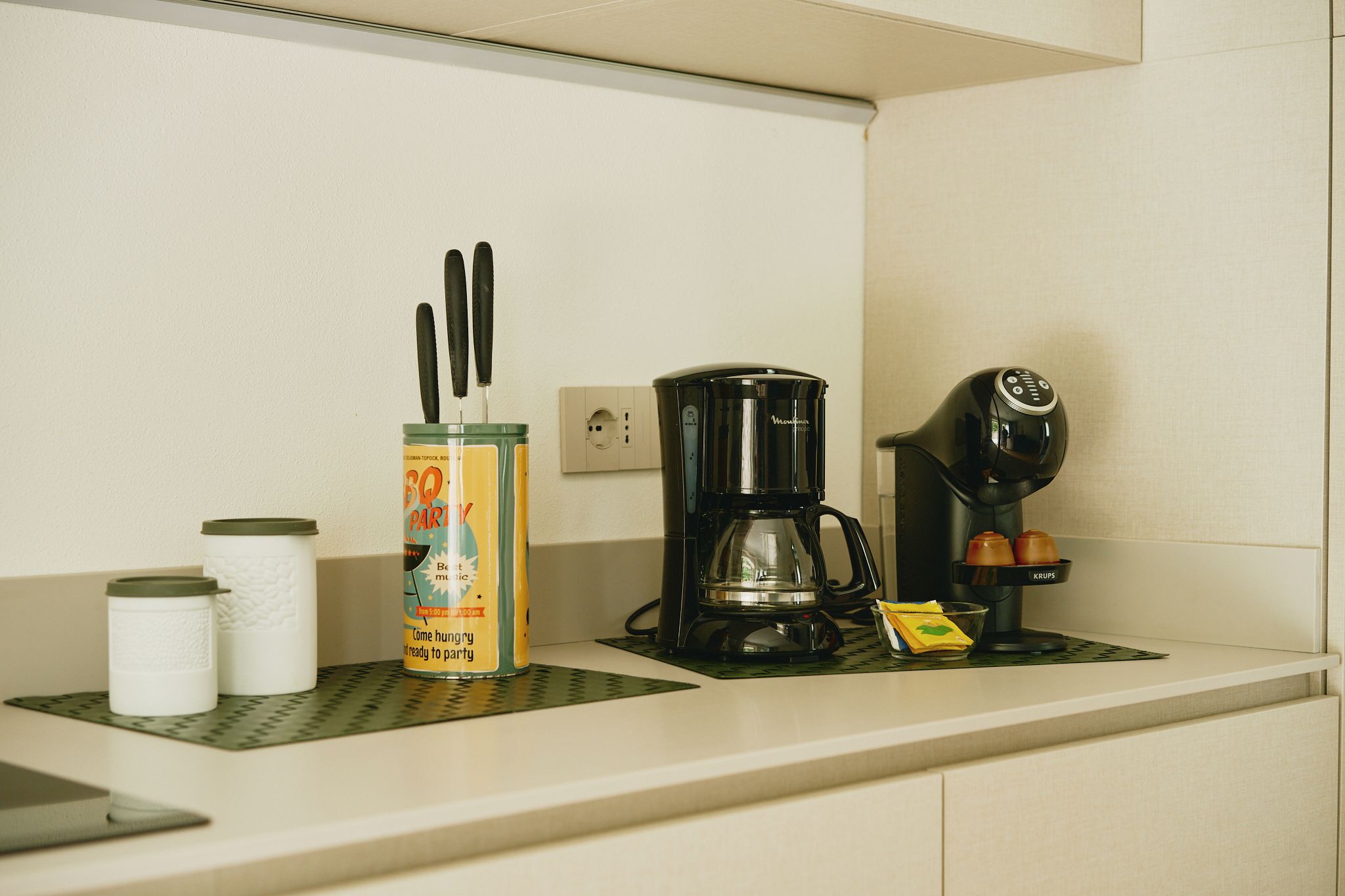 A kitchenette with a coffee maker, a canister with utensils, and a Krups coffee machine.