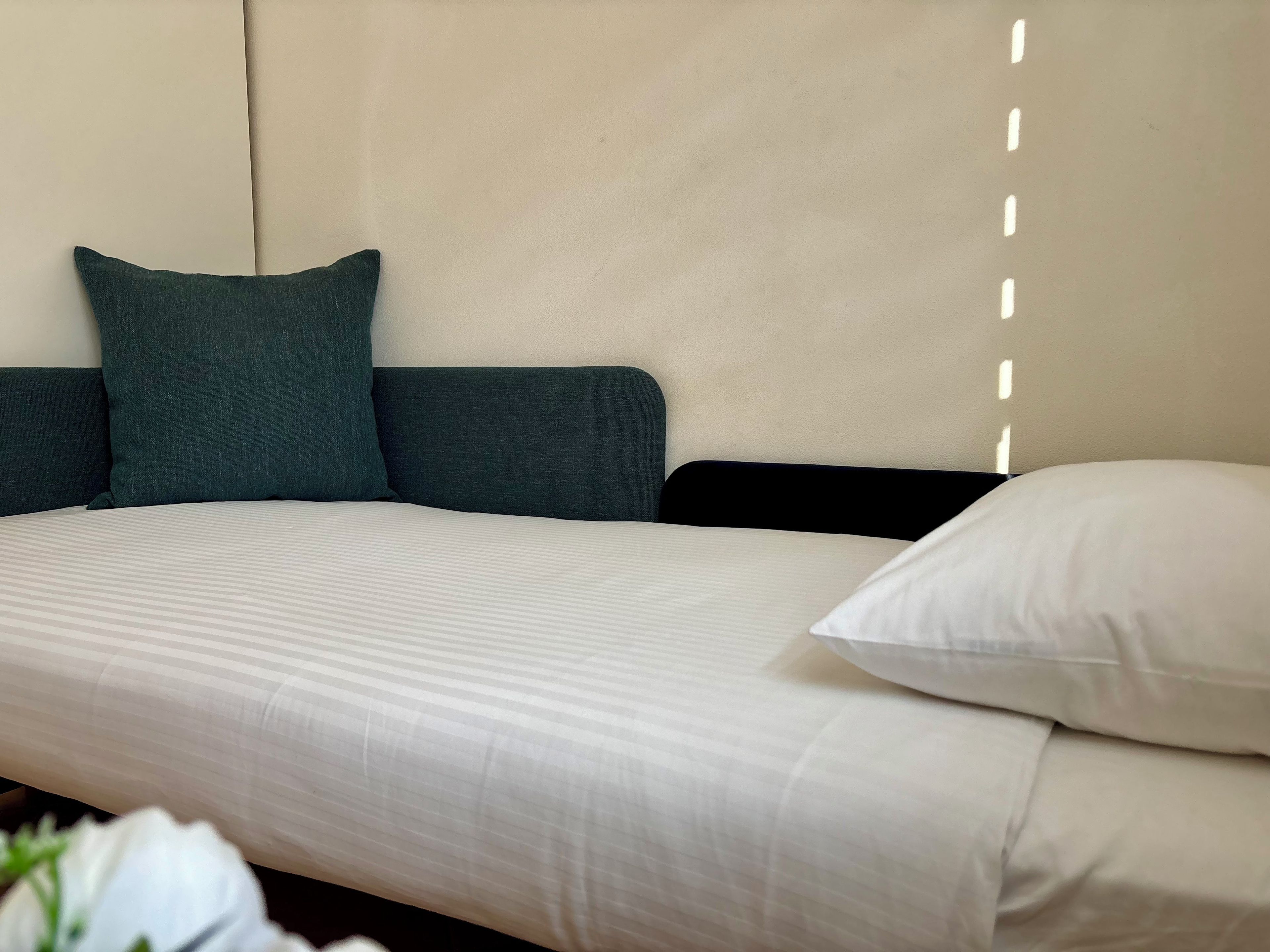 A bed with a striped bedspread, a dark green pillow, and a white pillow.