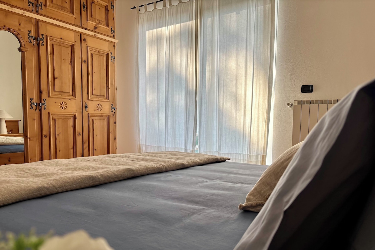A bedroom with a bed, wooden wardrobe, and a window with curtains.