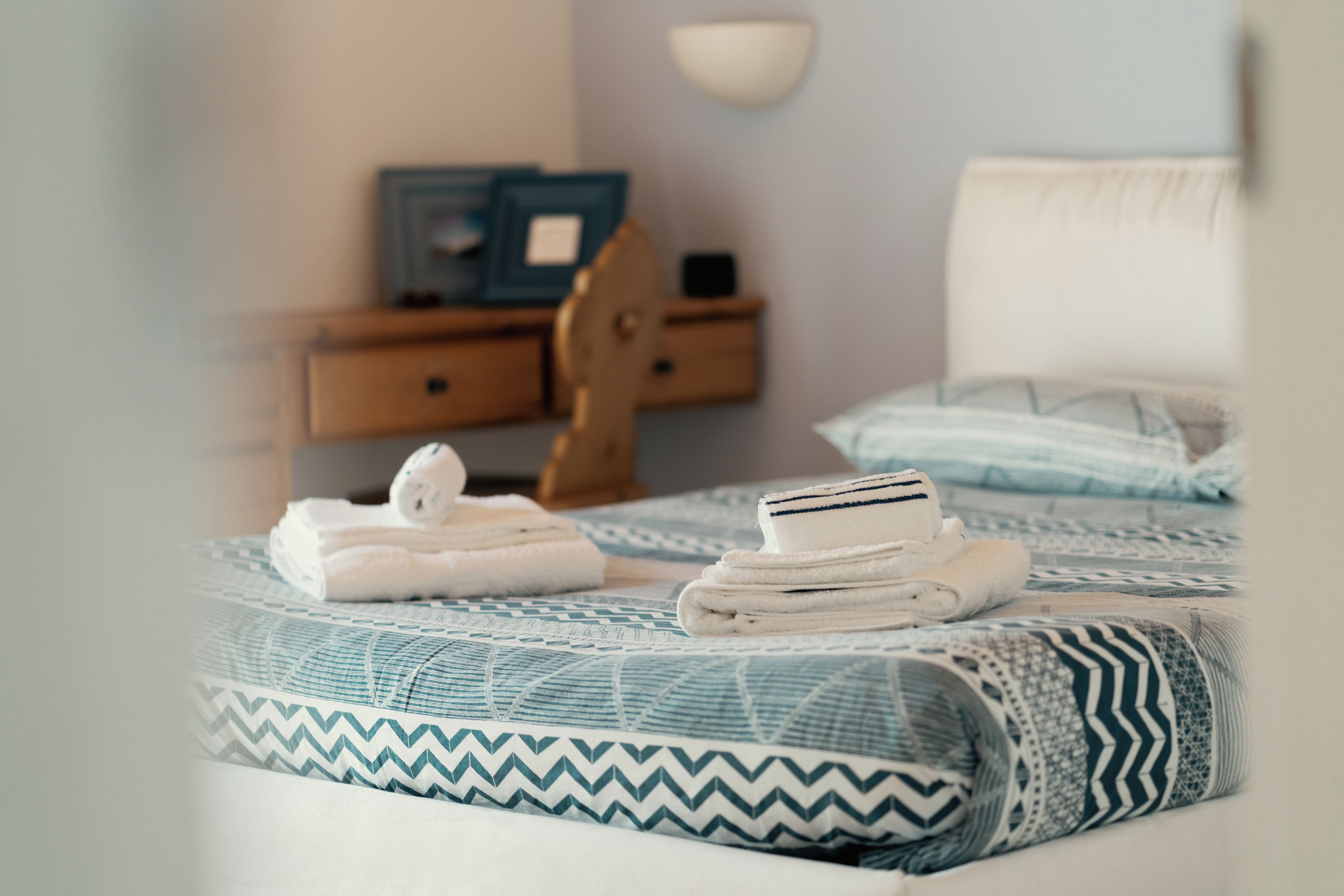 Un letto rifatto con una coperta a motivi, un comodino in legno con una lampada e una piccola sedia di legno.