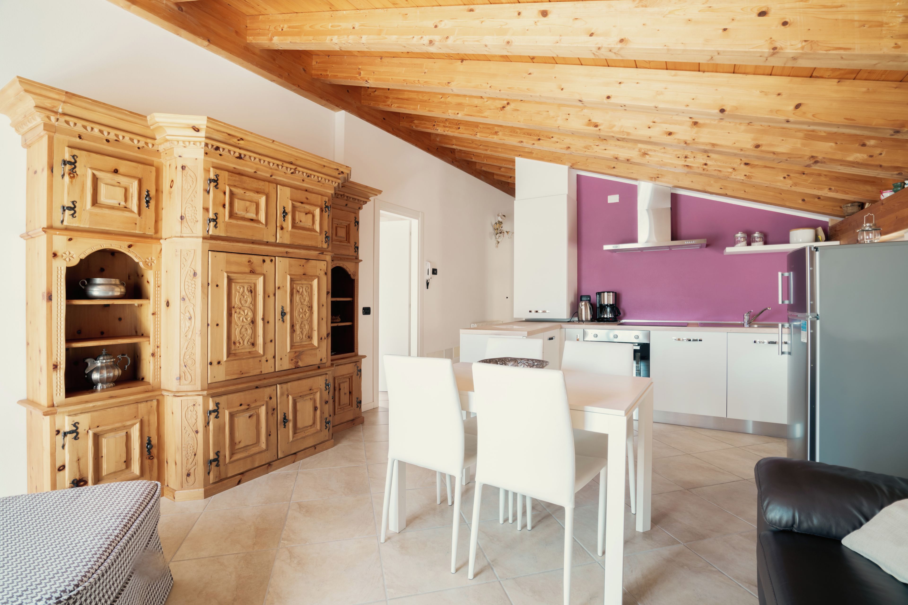 Une cuisine moderne avec des meubles en bois, un coin repas avec des chaises blanches et un mur d’accent violet.