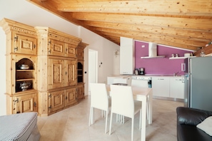 A modern kitchen with wooden cabinets, a dining area with white chairs, and a purple accent wall.