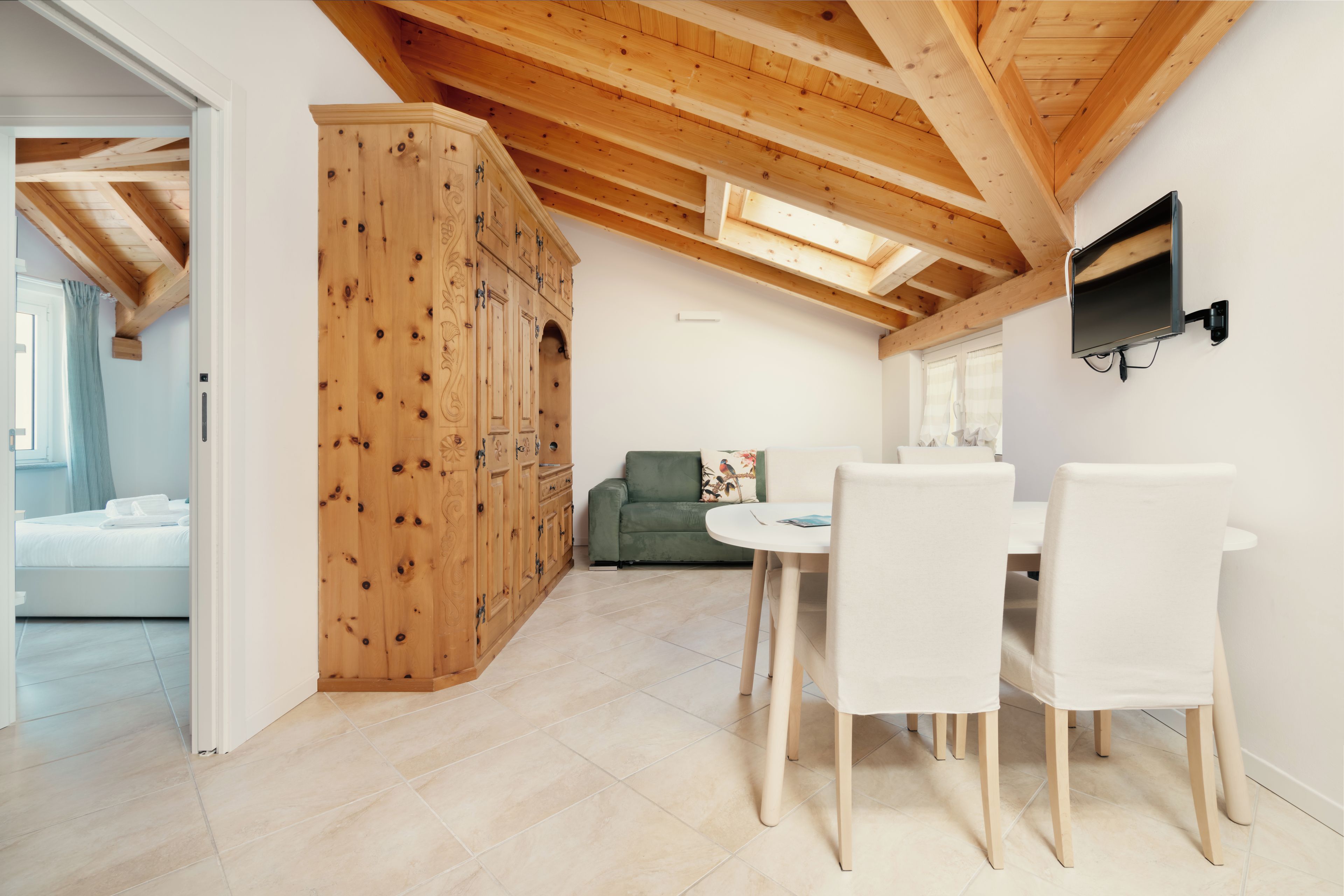 A modern interior with a dining area, wooden ceiling beams, and a green sofa.