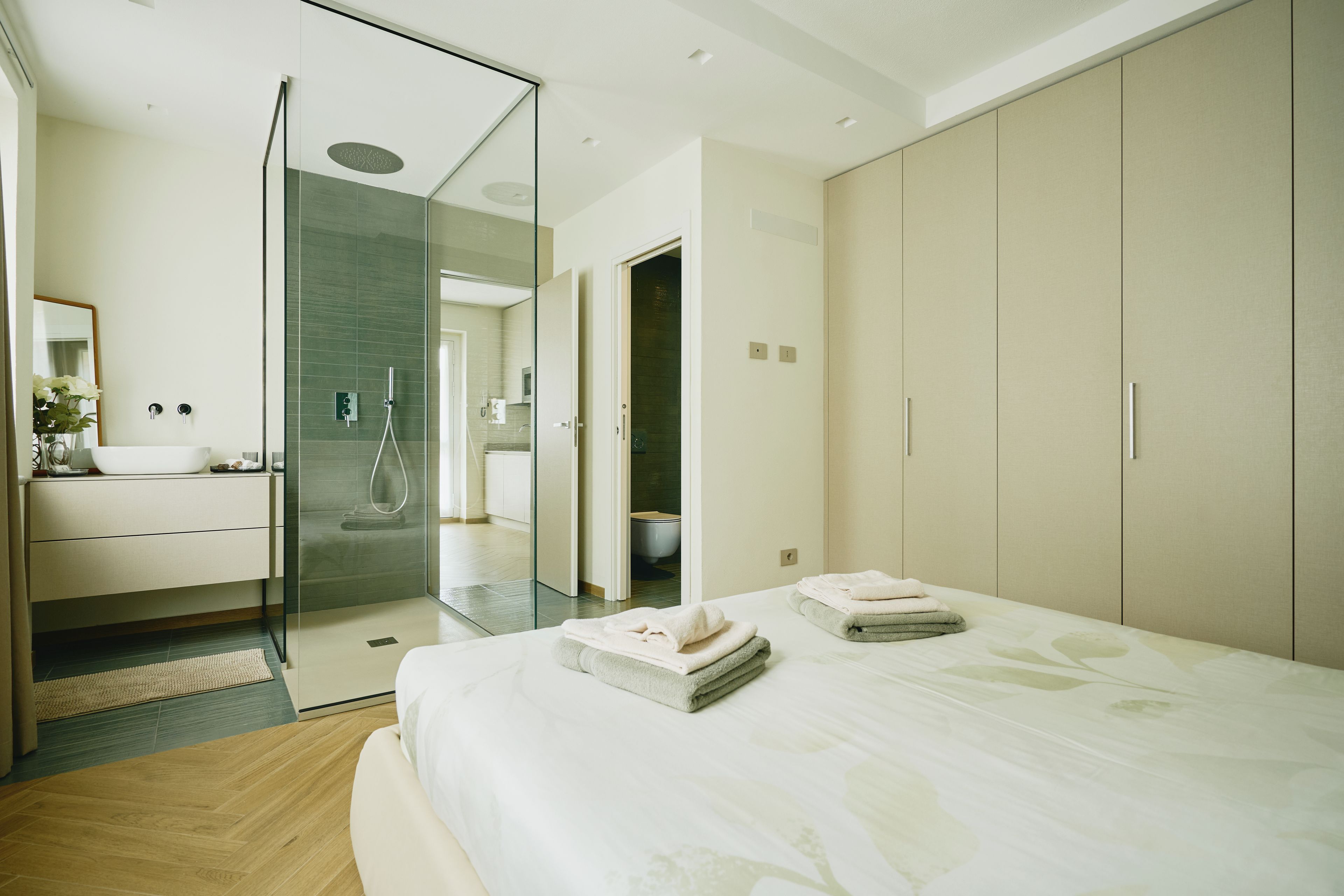 Un dormitorio moderno con una cama grande, cabina de ducha de vidrio y un baño minimalista.