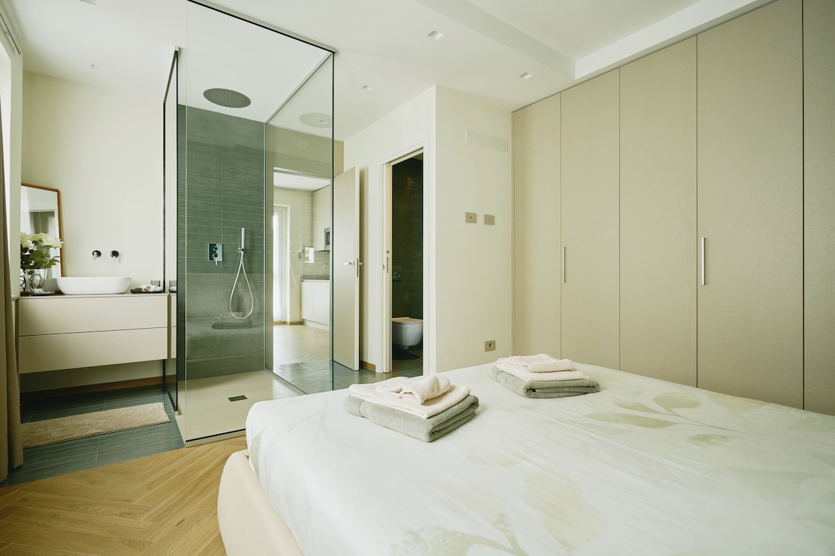 A modern bedroom with a large bed, a glass shower enclosure, and a minimalist bathroom.