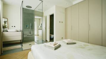 Un dormitorio moderno con una cama grande, cabina de ducha de vidrio y un baño minimalista.