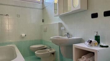 A bathroom with a bathtub, toilet, bidet, sink, and a towel rack with towels.