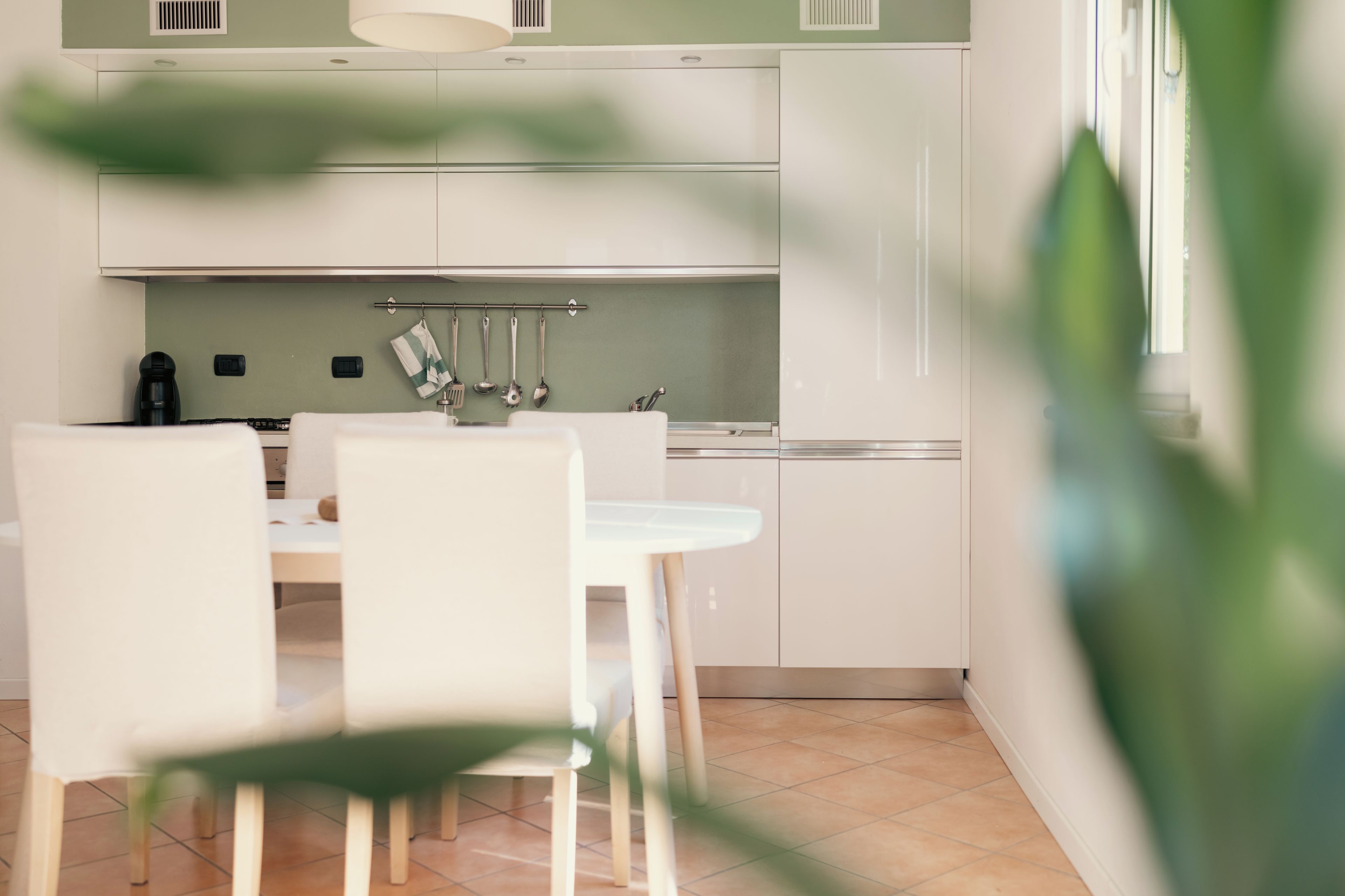 Une cuisine moderne avec des meubles blancs, une table à manger avec des chaises et un porte-ustensiles suspendu.