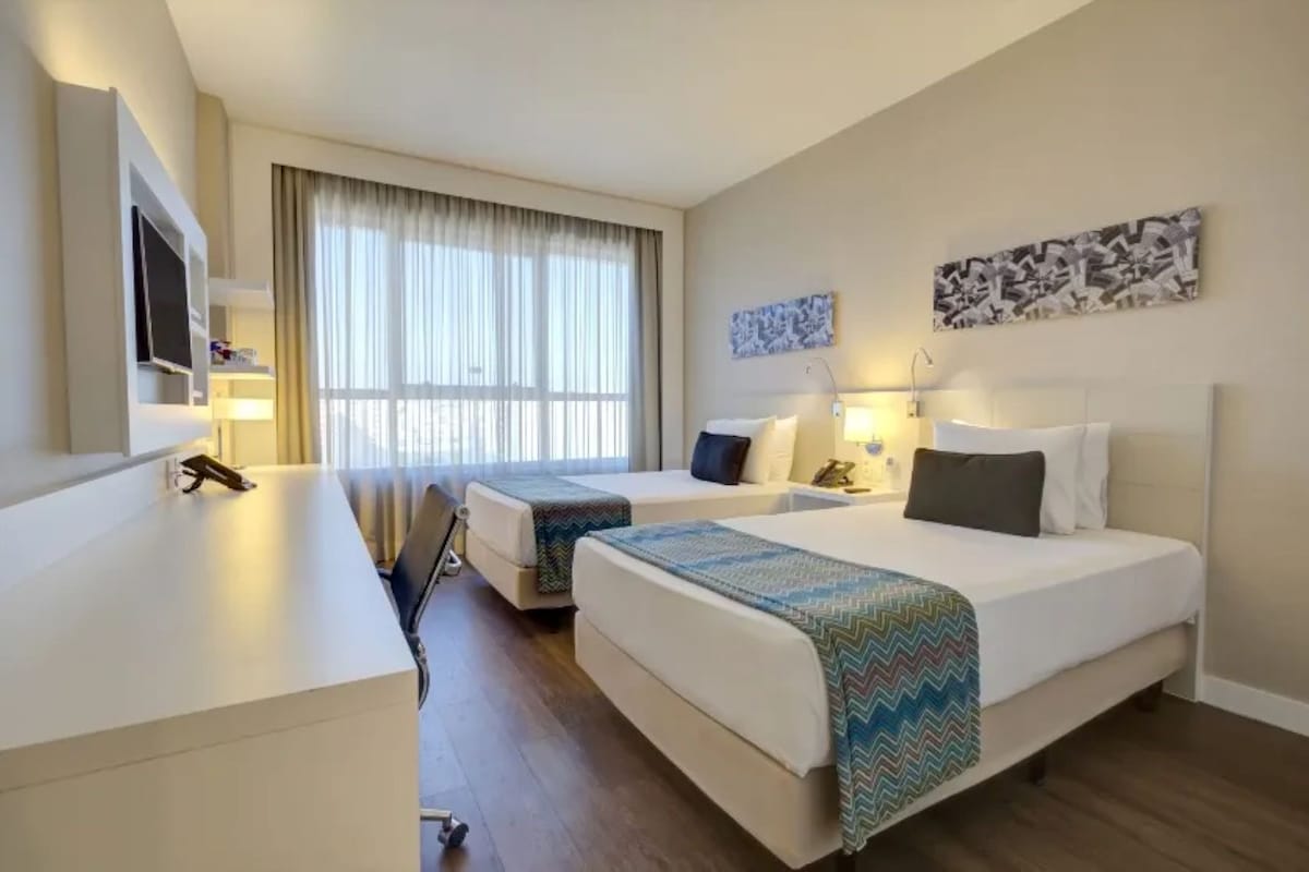 Habitación de hotel con dos camas, un escritorio, un televisor y obras de arte en las paredes.