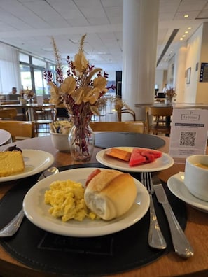 Una mesa de comedor con alimentos para el desayuno, como huevos revueltos, un panecillo y una rebanada de pastel.