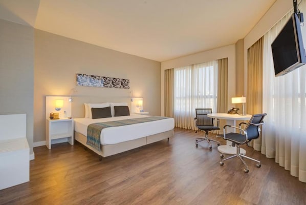 Una habitación de hotel con cama, mesitas de noche, escritorio con silla y televisor montado en la pared.