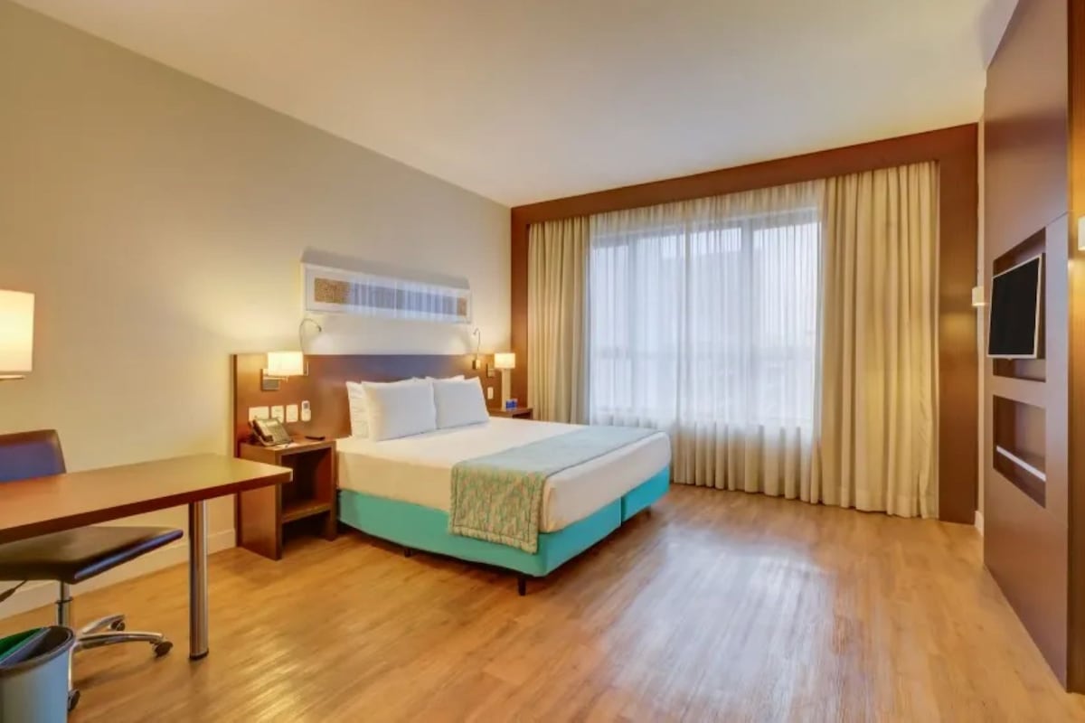 Una habitación de hotel con una cama, mesitas de noche, un escritorio y un televisor.