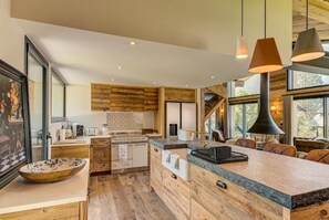A modern kitchen with wooden cabinetry, a central island, and a dining area with leather seating. - Beautiful chalet in heart of Chamonix sleeps 8-10, 4 bed/4 bath (+king sofa bed) (Chamonix-Mont-Blanc)