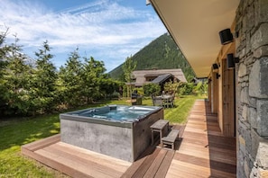 A hot tub on a wooden deck with a stone wall and a mountain in the background. - Beautiful chalet in heart of Chamonix sleeps 8-10, 4 bed/4 bath (+king sofa bed) (Chamonix-Mont-Blanc)