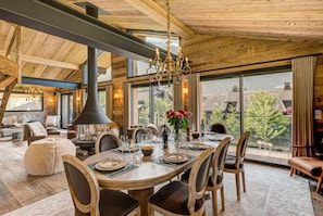 A spacious dining area with a large wooden table set for a meal, surrounded by chairs, and a chandelier above. - Beautiful chalet in heart of Chamonix sleeps 8-10, 4 bed/4 bath (+king sofa bed) (Chamonix-Mont-Blanc)
