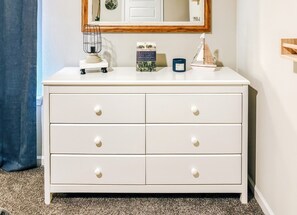 A white dresser with four drawers, a small lamp, a book titled 'Legends of Mississippi,' and a small decorative sailboat. - The Coastal Chapter—Spacious 3-Bedroom Home in Ocean Springs (Ocean Springs)