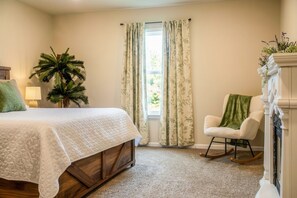 A bedroom with a bed, a potted plant, a rocking chair, and a fireplace. - The Coastal Chapter—Spacious 3-Bedroom Home in Ocean Springs (Ocean Springs)