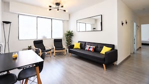 A modern living room with a black leather sofa, wooden chairs, a dining table, and a large window. - CasaGoa Madrid | 5-bedroom home near Madrid Río (madrid)