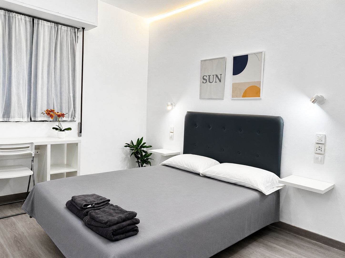 A modern bedroom with a large bed, a desk, and a window with curtains.