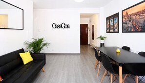 A modern living room with a black sofa, a dining table with chairs, a potted plant, and a wall-mounted sign reading 'CasaGoa'. - CasaGoa Madrid | 5-bedroom home near Madrid Río (madrid)