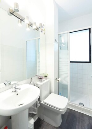 A modern bathroom with a white sink, mirror, toilet, and shower. - CasaGoa Madrid | 5-bedroom home near Madrid Río (madrid)