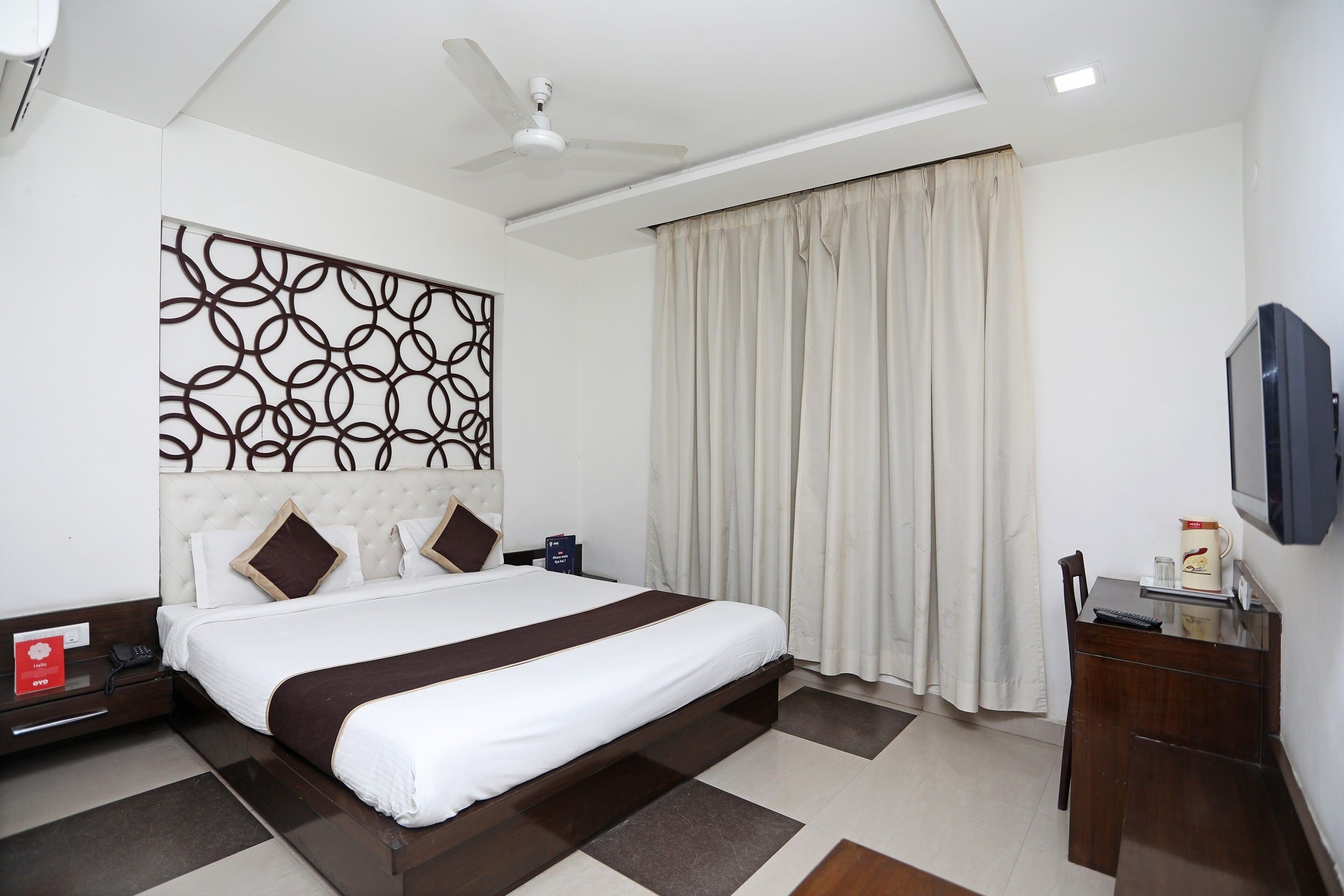 Una habitación de hotel con cama, mesita de noche, televisor y ventilador de techo.