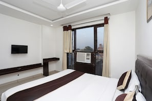 A hotel room with a bed, a television, a window with curtains, and an air conditioning unit. - Capital O Taj Castle (Agra)