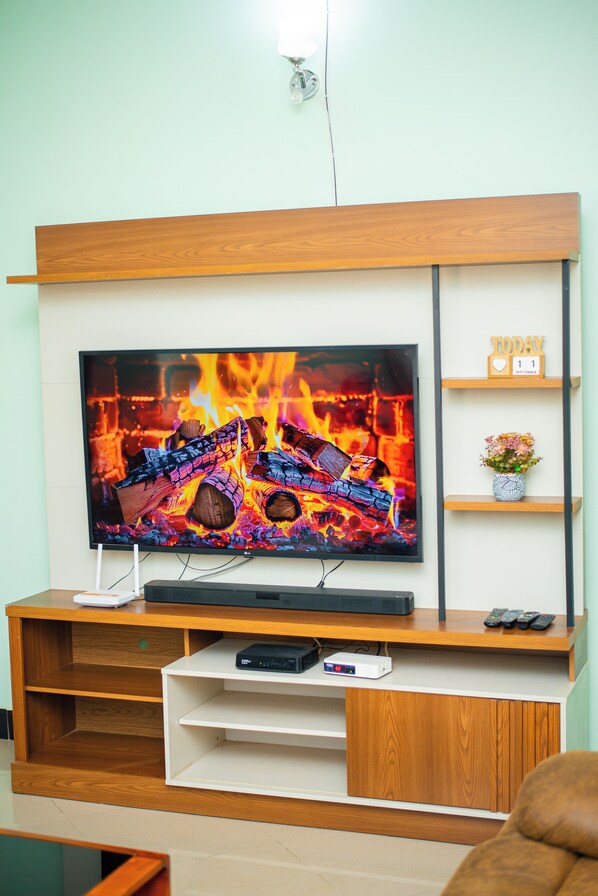 A flat-screen TV mounted on a wooden entertainment center with a shelf below displaying a date and a heart-shaped decoration.