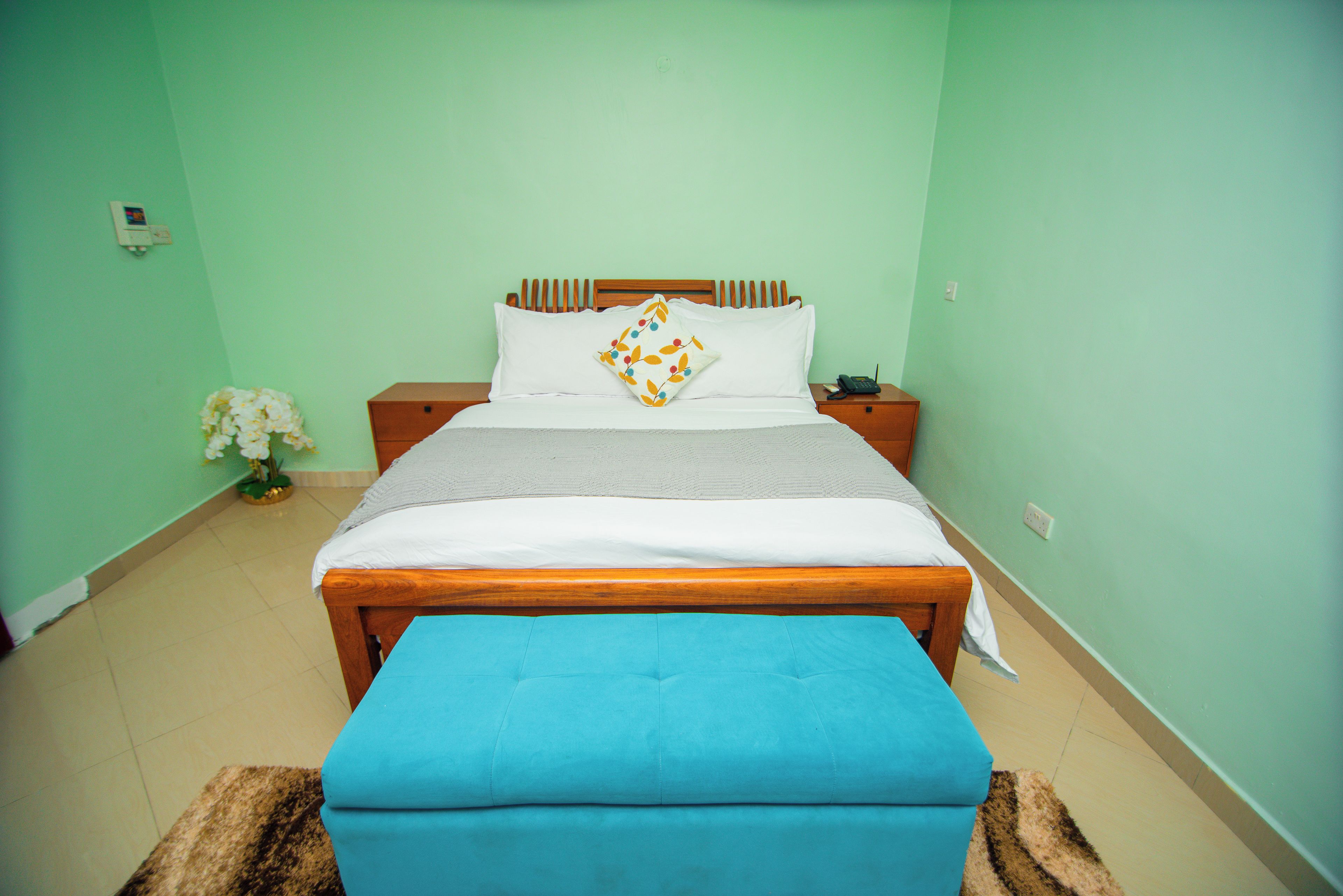 Quarto com cama, mesa de cabeceira e um banco azul.