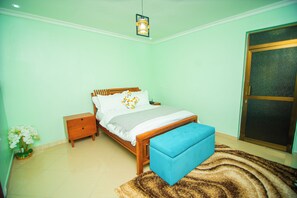 A bedroom with a bed, bedside tables, a bench, a wall-mounted light, and a door.
