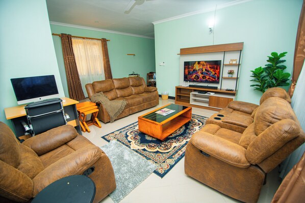 A living room with a sofa set, a coffee table, a flat-screen TV, and a television on a stand.