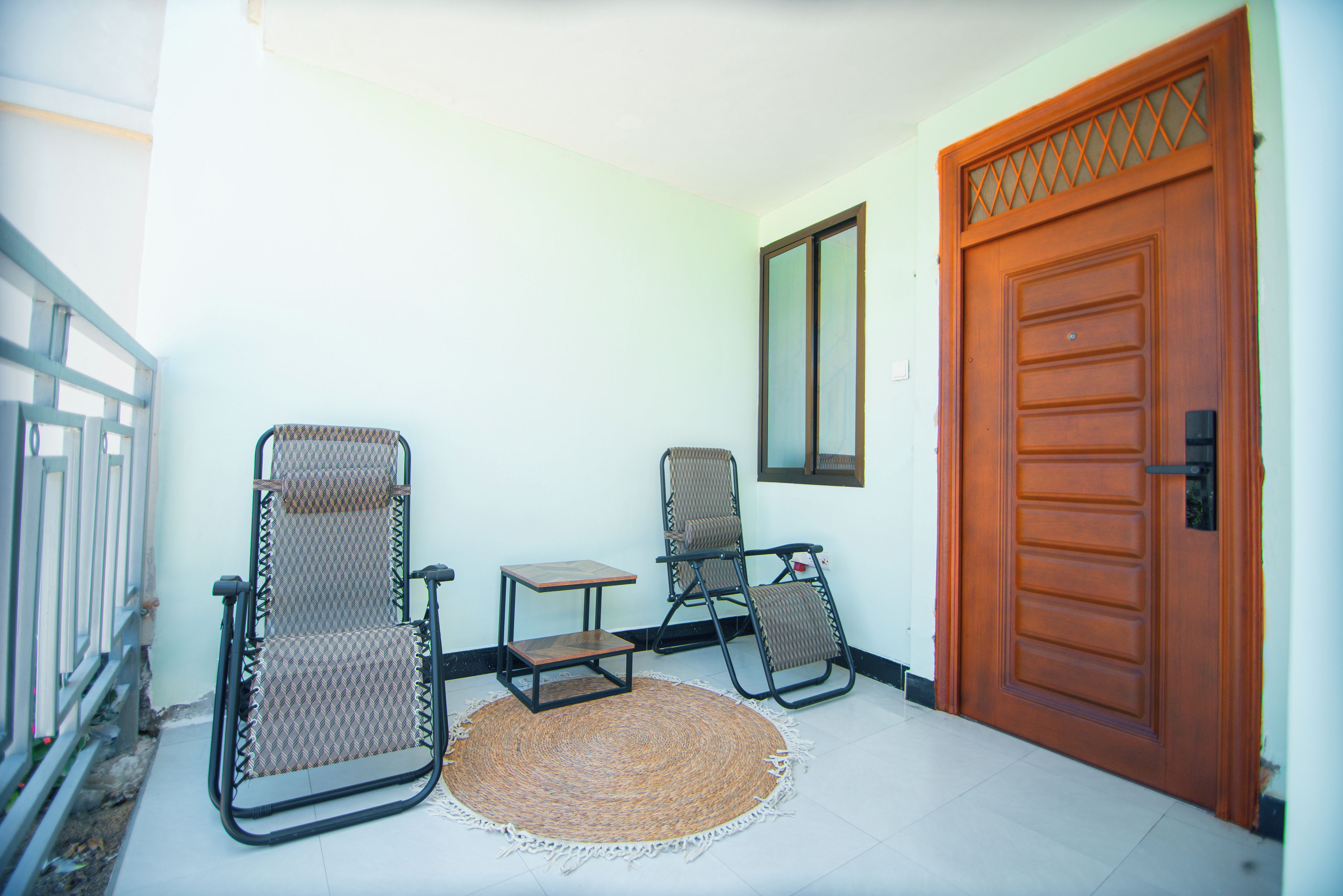 Una habitación con dos sillas, una mesita, un tapete tejido y una puerta de madera.