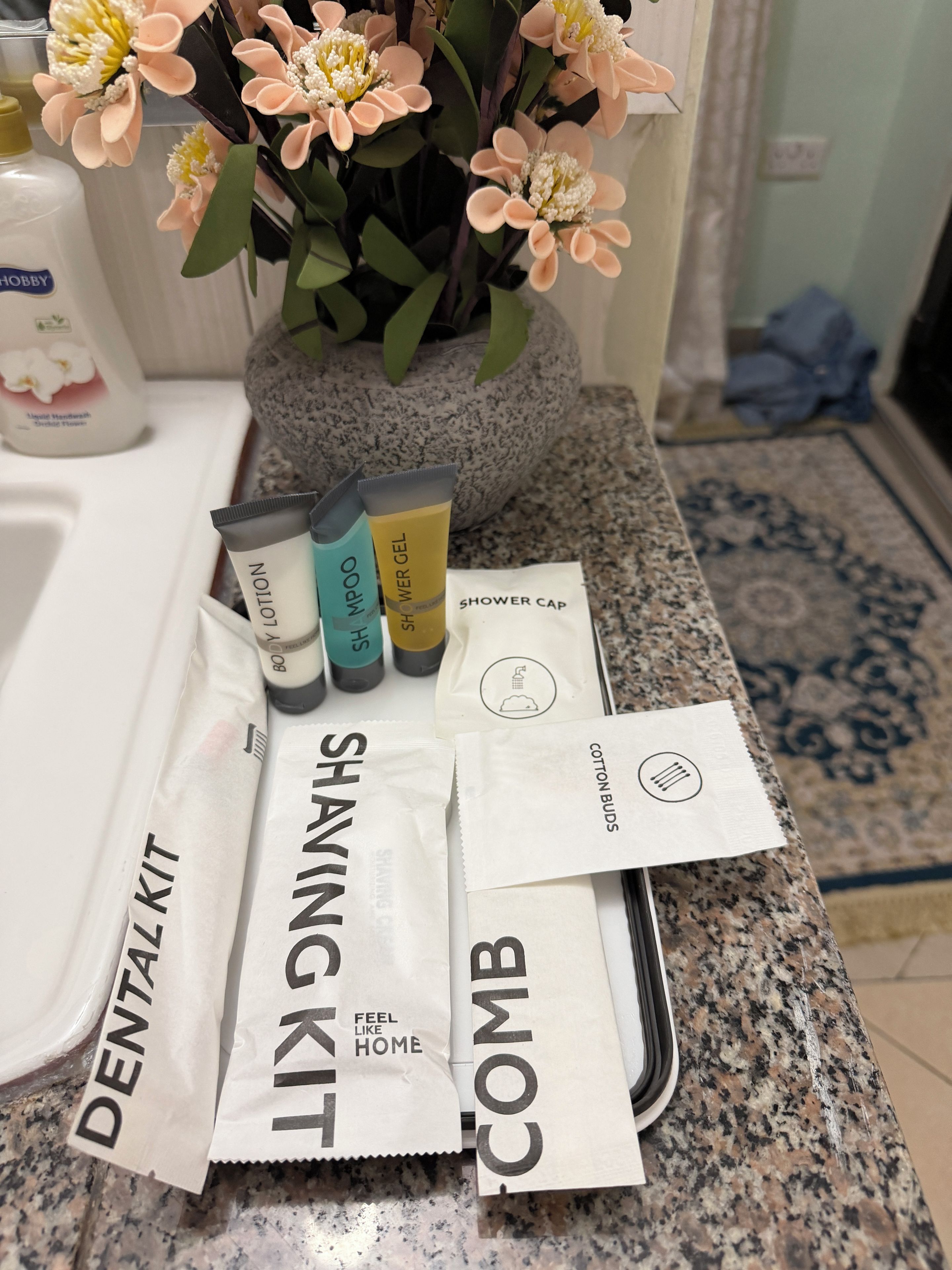 A bathroom counter with a tray containing toiletries, a shower cap, cotton buds, and a dental kit.